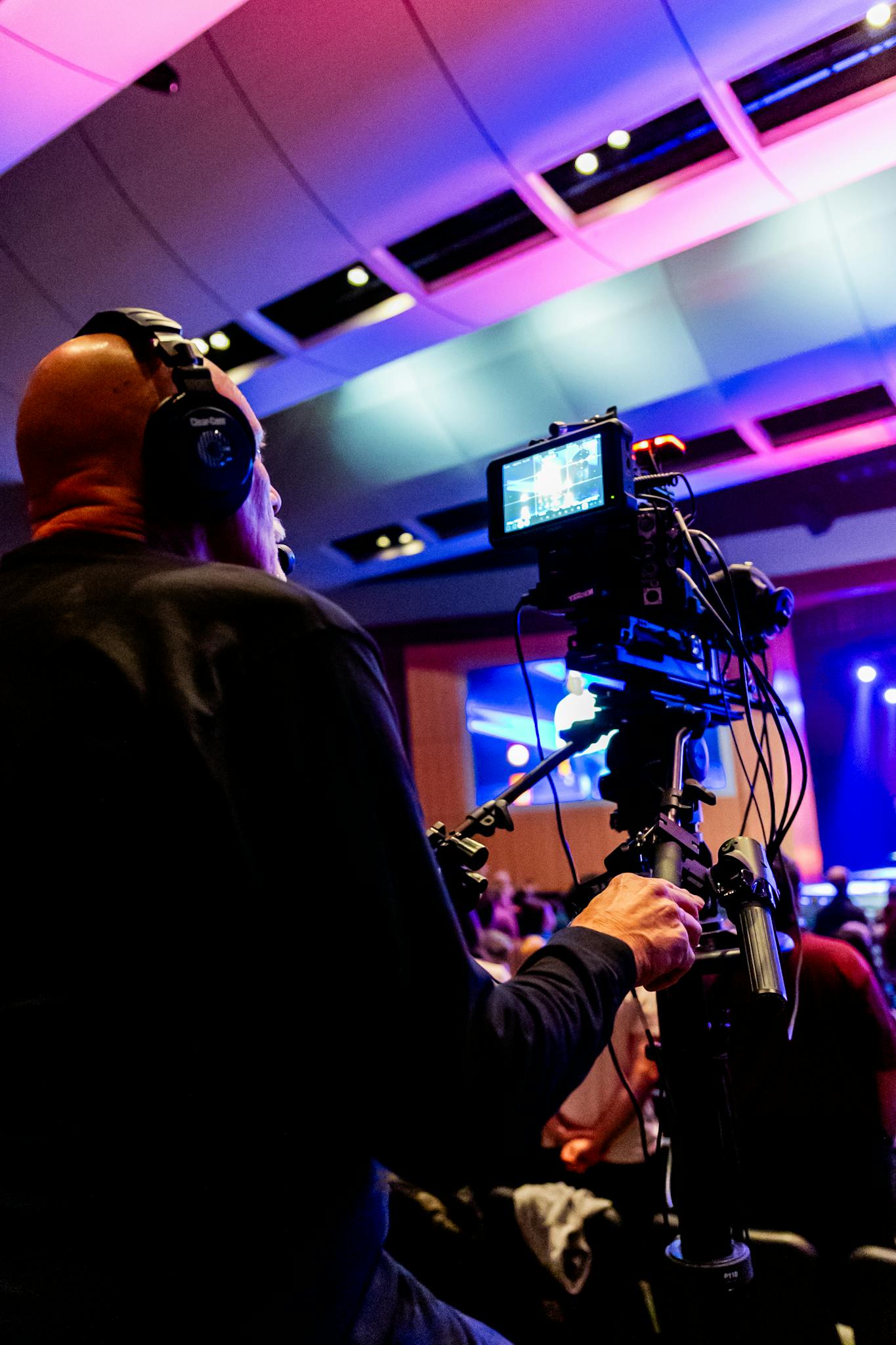 Cameraman capturing a live indoor event with vibrant stage lighting and a bustling audience.